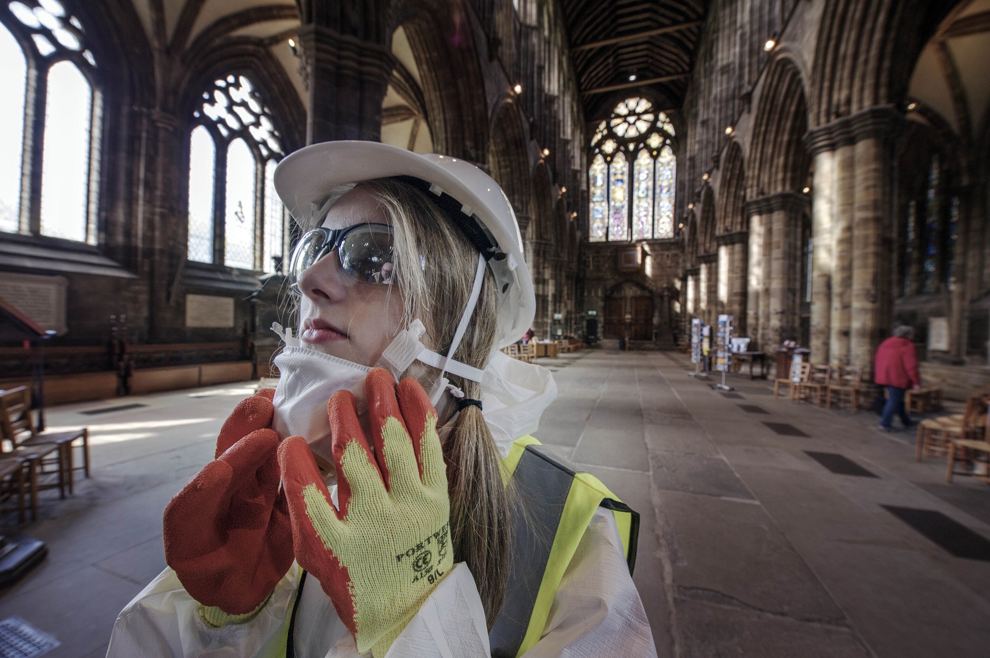 A person with long blonde hair wearing protective gear, standing inside Glasgow Cathedral