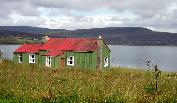 Corrugated iron house with green walls and red roof next to loch