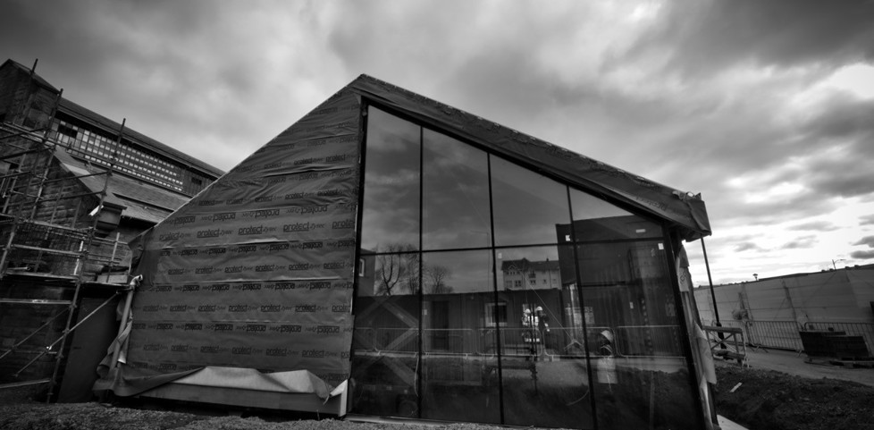 Black and white exterior of The Engine Shed under construction with glass and brick wall