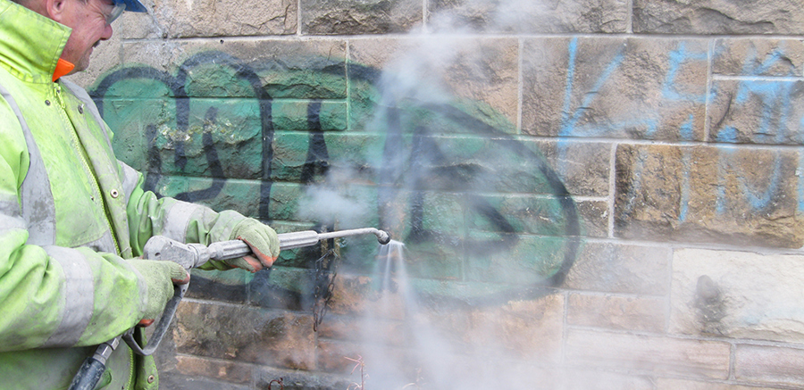 A person spraying something onto a stone wall to remove graffiti