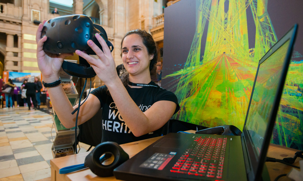 Someone smiling whilst holding up a VR headset with a point cloud image in the background
