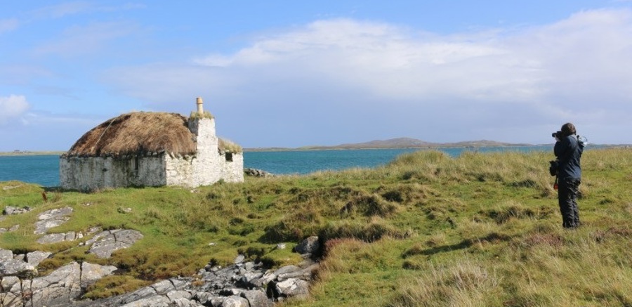 A person taking a photograph of a white thatched cottage by the sea