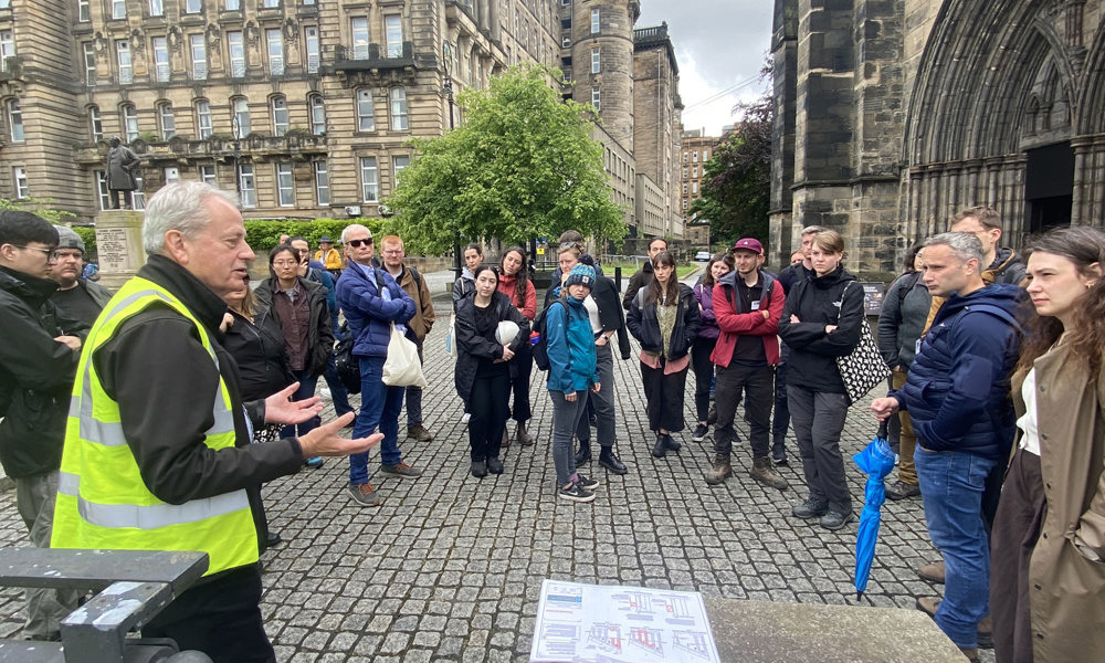 A group of people standing outside the historic, stone Glasgow Cathedral, gathered around as a person gives them a talk