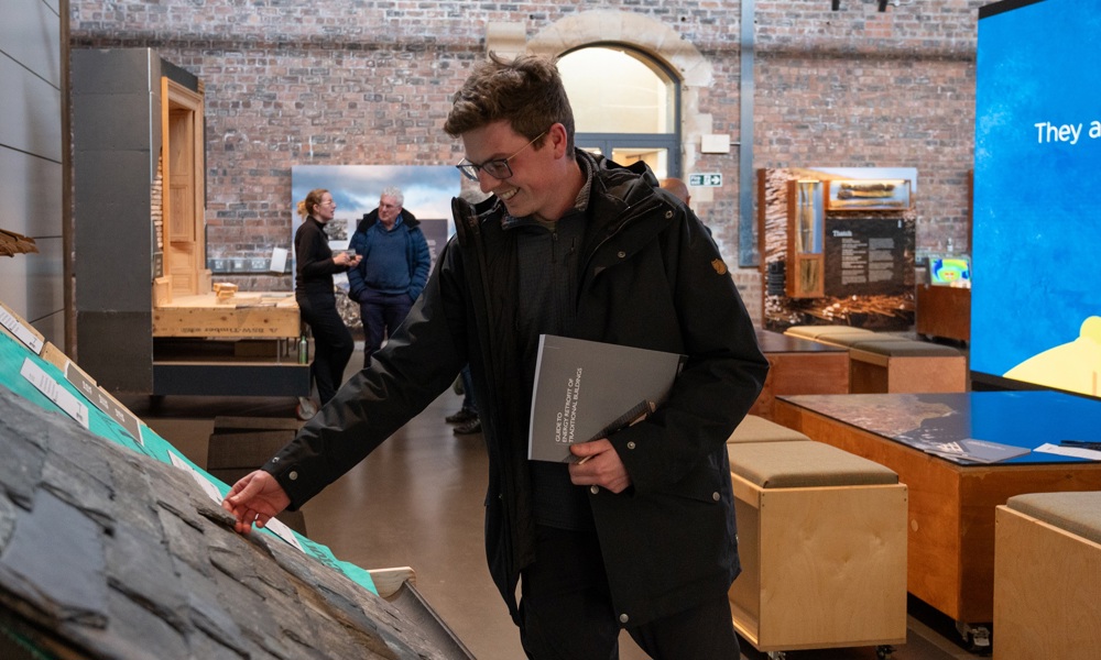 A person is holding the publication 'Guide to Energy Efficiency' and examining the model of a traditional roof in the Engine Shed.