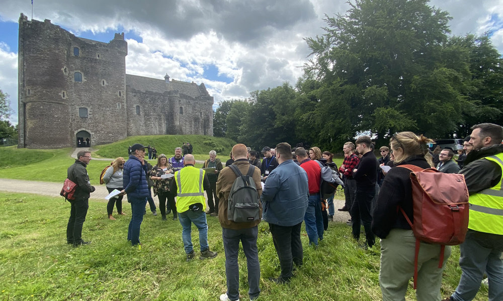 A large group of people standing outside Doune Castle on the grass